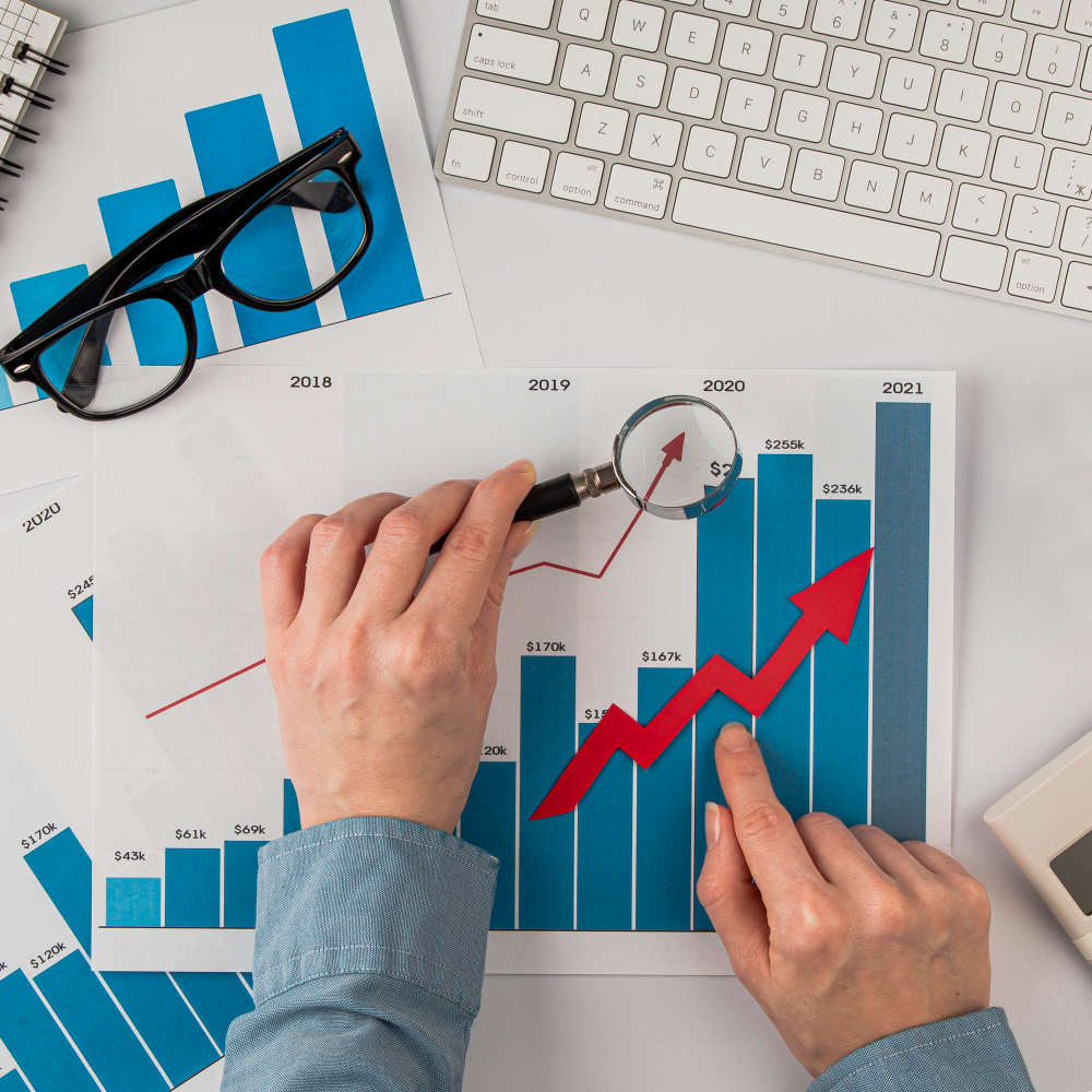 top-view-office-desk-with-growth-chart-hands-holding-magnifying-glass